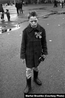 Lenin Square, Minsk. A boy in rubber boots and tattered pants stands in a puddle, with a black eye and a pioneer badge, November 7, 1989.