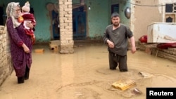 An Afghan woman holds her child as her husband salvages their belongings outside their flooded house in northern Afghanistan.