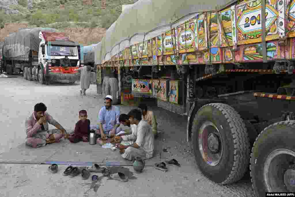 Truck drivers and young children drink tea near their parked vehicles. Pakistan is in the grip of an economic downturn, while Afghanistan is facing a catastrophic humanitarian crisis under the leadership of the Taliban, which took control in mid-2021.&nbsp;