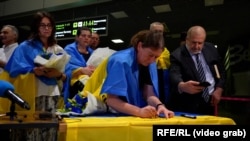 Natalia Zakharenko signs a Ukrainian flag at a homecoming ceremony in Kyiv early on June 29