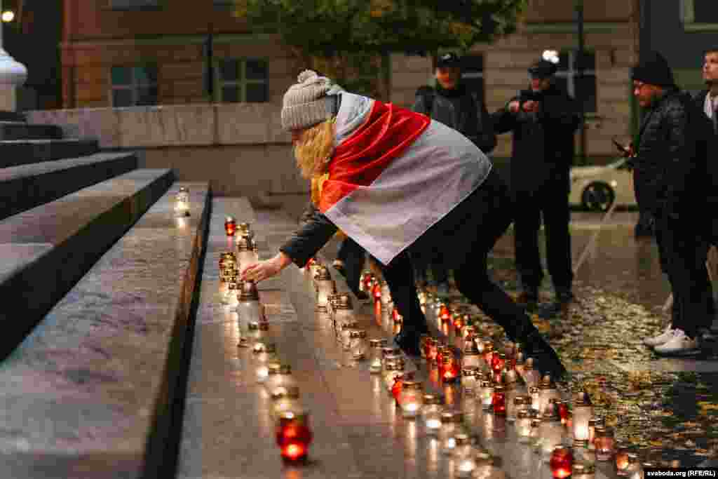 A woman wearing the white-red-white flag of the Belarusian Democratic Republic places a candle on the steps of Vilnius city hall in Lithuania on October 29. A total of 132 candles were lit in memory of Belarusian intellectuals, poets, politicians, artists, and scientists who were executed on October 29&ndash;30, 1937.&nbsp;