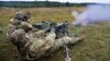 Two soldiers fire an M-249 light machine gun at an unknown location.