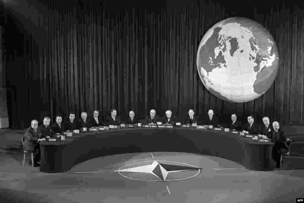 A NATO conference in Paris in 1957 behind the NATO emblem which was adopted in 1953. NATO&#39;s flag features a dark blue, representing the Atlantic Ocean, with a compass rose representing the direction toward peace, and a circle symbolizing unity.&nbsp;&nbsp;