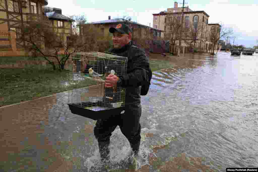 A man carries a cage with a parrot while walking along a flooded street following a storm in Yevpatoria.