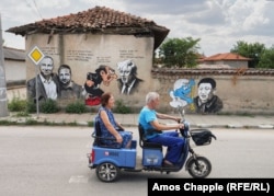 A local couple rides past a wall featuring political figures interacting with cartoon characters in Staro Zhelezare on August 6.