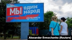 Women walk past a billboard displaying pro-Russian slogans in the Russian-occupied city of Melitopol in the Zaporizhzhya region in early August. The billboard reads: "We are one people. We are together with Russia."