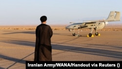 An Iranian cleric stands near a drone during a military exercise in an undisclosed location in Iran. The United States has placed sanctions on companies involved in the research and development of Iranian drones.