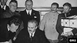 Foreign Minister Vyacheslav Molotov signs the pact. Behind him are Ribbentrop and Stalin 