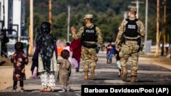 U.S. military police walk past Afghan refugees at the Ft. McCoy U.S. Army base in Wisconsin on September 28.