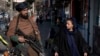 A Taliban security officer stands guard on a Kabul street as a woman passes by. (file photo)