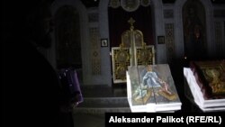 Priest Andriy Dudchenko tries to shine light on icons painted on ammunition boxes by Ukrainian artists Oleksandr Klymenko and Sofia Atlantova.