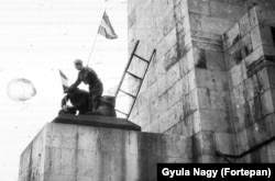 After the statue of the Soviet soldier is torn down, cameraman Miko Jozsef attaches a Hungarian flag to the remaining boots of the statue with the help of a young soldier.