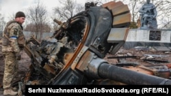 A Ukrainian serviceman inspects the remains of a destroyed Russian tank in the Kyiv region.