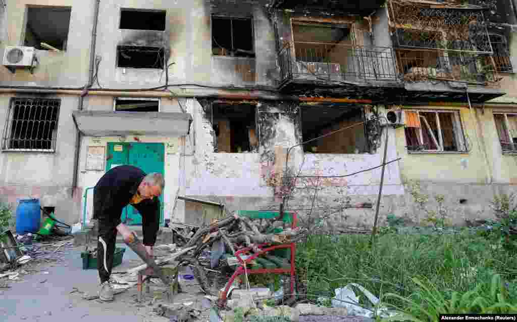 A local resident cuts firewood outside a damaged residential building on May 12.&nbsp;Under Russian control the city is struggling to restore basic services such as electricity and water.