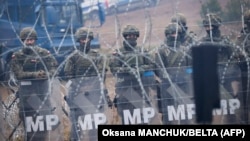 Polish soldiers stand behind a barbed-wire fence on the Belarusian-Polish border as they watch migrants camping on the Belarusian side in the Hrodna region on November 14. 