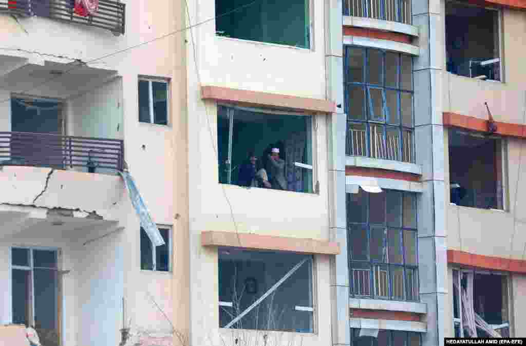 Afghan men look out a damaged window of an apartment that faces the scene.