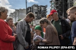 Residents gather to receive humanitarian aid in front of residential buildings damaged during the Russian attack.