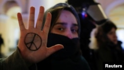 A demonstrator shows a peace symbol painted on her hand as she stands next to a riot police officer during an anti-war protest against Russia's invasion of Ukraine in St. Petersburg on March 2.