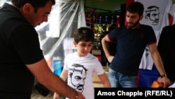 A youngster trying on a T-shirt with Nikol Pashinian's face and a pirated version of the "Duxov" logo at a market in Yerevan.