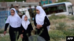 Afghan schoolgirls walk past a damaged military bus after a May 26 suicide attack in Kabul.