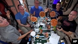 American Mark Vande Hei (left), Russian Sergei Ryazansky, Italian Paolo Nespoli, American Joe Acaba, and American Randy Bresnik display the results of their made-from-scratch pizza pies on the International Space Station.