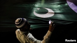 A supporter of the religious party Jamaat-e Islami takes pictures with a mobile phone as he holds Pakistan's national flag during an election campaign rally in Karachi.