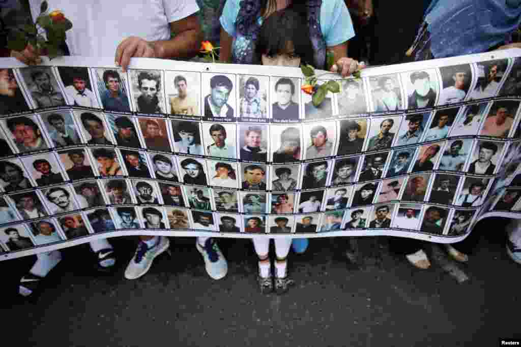 A Bosnian child holds a placard with portraits of victims of the 1995 Srebrenica massacre while a truck, one of three carrying 409 coffins of newly identified victims of the massacre, passes. (Reuters/Dado Ruvic)