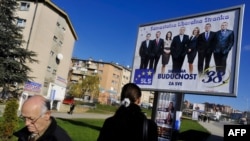 Ethnic Albanians walk past an electoral billboard featuring Serb leaders of the Independent Liberal Party in Pristina on December 8.