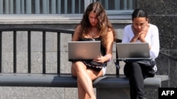 Young women work on laptops while waiting for a bus in Moscow.