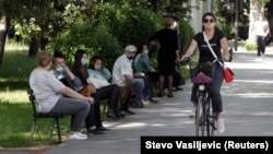 A women rides a bicycle past people waiting for a bus in Podgorica on May 25. 