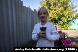 Toma holds part of the shell in a neighbor's yard, where her sister and brother were injured in Maryinka.