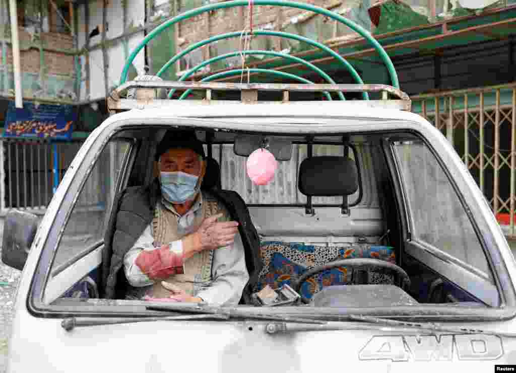 An injured man sits inside his damaged vehicle.