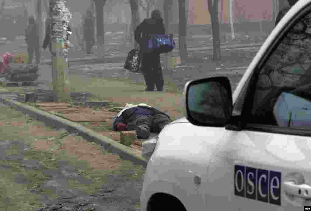 An observer&#39;s car from the Organization for Security and Cooperation in Europe (OSCE) stands near a victim&#39;s body on a street in Mariupol.