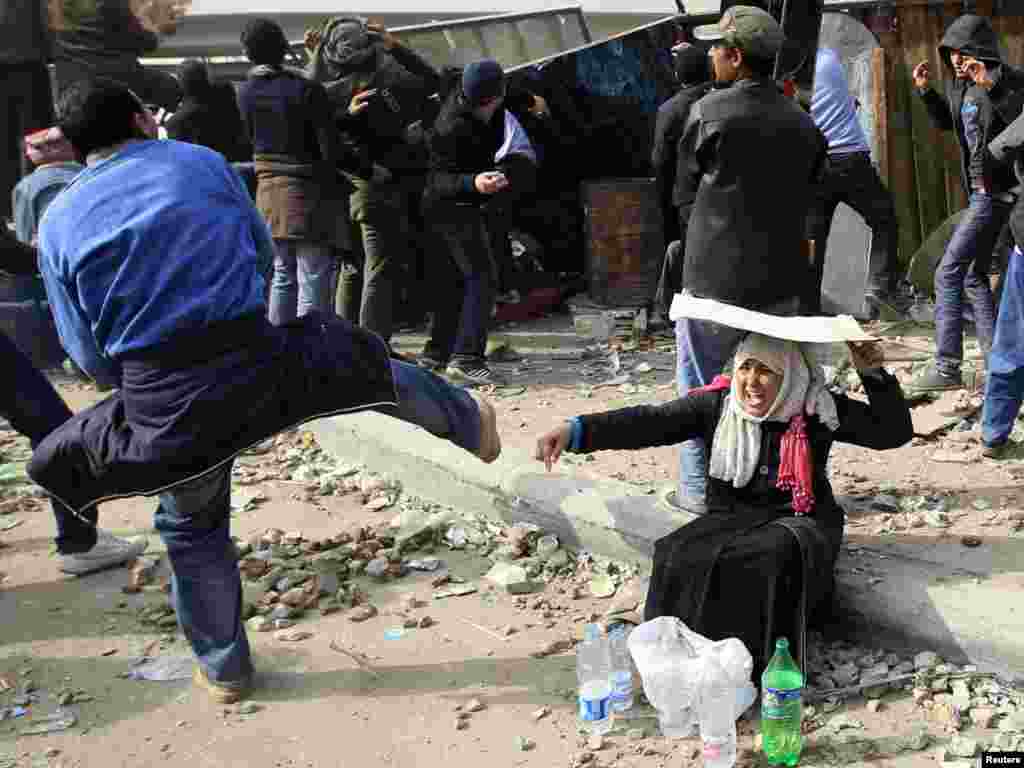 A woman opposition supporter takes shelter while providing water during rioting with Mubarak supporters.