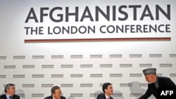 Afghan President Hamid Karzai (standing) shakes hands with British Foreign Minister David Miliband after making a speech at the opening session of the Afghanistan Conference in London on January 28.