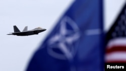 The U.S. and NATO flags flutter as a U.S. Air Force F-22 Raptor fighter jet flies over the military air base in Siauliai, Lithuania, on April 27.