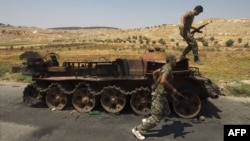 Syrian rebel fighters are pictured next to a burnt-out army tank in the northern town of Atareb, 25 kilometers east of Syria's largest city, Aleppo, on July 31.