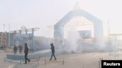 In this still image taken from video acquired by Reuters, people walk past a destroyed stage in the Kazakh town of Zhanaozen