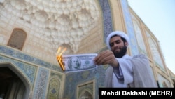 Another Qom protester burns a U.S. dollar to protest economic hardships on August 16.