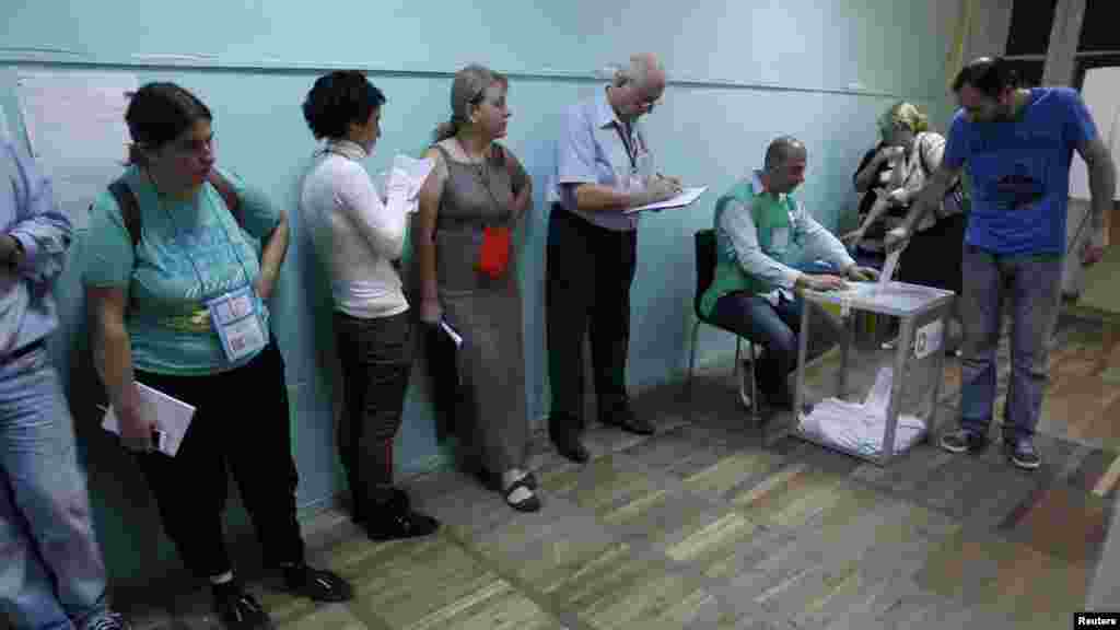 Observers line up in front of a wall, while a voter casts his ballot, at a polling station in Tbilisi.