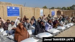 Afghans sit beside sacks of food grains distributed as aid by the World Food Program in Kandahar on October 19.