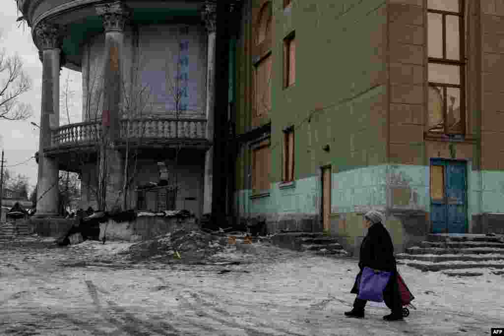 A woman walks with a trolley near a damaged cultural center in the Ukrainian town of Bilytske, in the Donetsk region. 