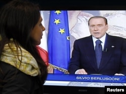 A woman watches a television screen showing former Prime Minister Silvio Berlusconi as he reads his speech during a farewell video in a shop in Cisternino, Italy.