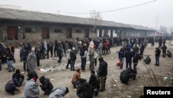 Migrants eat as others stand in line to receive free food outside a derelict customs warehouse in Belgrade. (file photo)