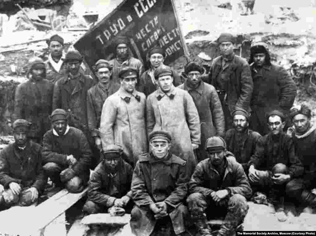 Shock workers and officials from the Belomorkanal camp visiting a forest in Vaidai in 1932, posing in front of a banner that read: &quot;Labor in the U.S.S.R. is a matter of Honor, Glory, Valor, and Heroism.&quot;