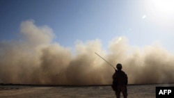 A U.S. Marine stands guard as a landing helicopter churns up a cloud of dust in Marjah, Helmand Province.