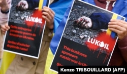 Protesters hold signs as they gather near the LUKoil headquarters in Brussels on May 13 to call for a boycott. LUKoil, Russia's second-largest oil company, produces 2 percent of the world's crude oil.