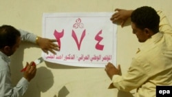 Iraqi men put up election posters on a wall on a street in Al-Najaf.