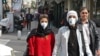 People wearing protective masks walk along a street in the Iranian capital, Tehran, on February 24.