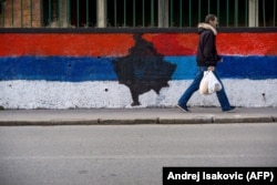 A pedestrian walks past a wall painted in the colors of the Serbian national flag with a map of Kosovo in the middle, in Belgrade on February 12, 2018.